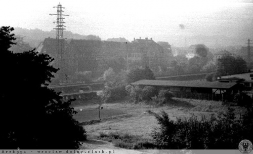 Wykopane z archiwum zdjęcie przedstawiające zabudowę ulicy Bolesława Chrobrego w roku 1965. Nieco bliżej ulica Kolejowa (jadšcy Żuk) oddzielona od ulicy Chrobrego żywopłotem. Za nim niewidoczne, dawne torowisko kolejowe. W miejscu widocznej szopy stoi...